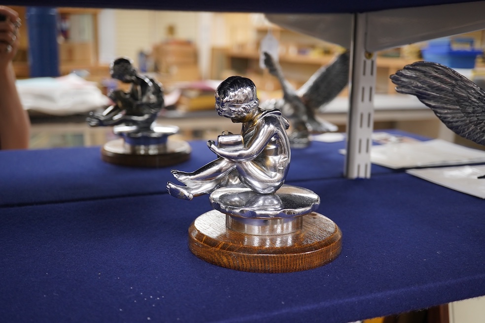 Two chrome car mascots, one in the form of an eagle stamped Finnigans London, wingspan 26cm, and the other of a classical child writing, mounted on a substantial radiator cap and oak base. Condition - fair to good, some